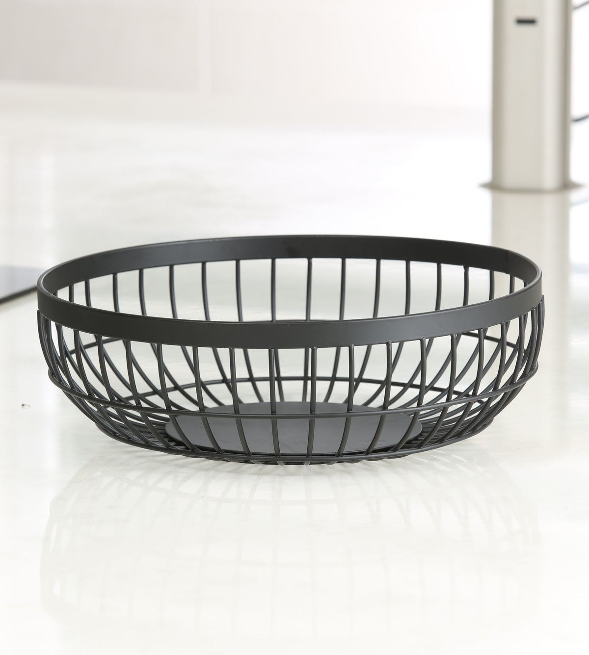 Empty matte black round wire fruit basket seen from the side, showing the crossed-wire lattice sides, wide flat rim band and solid round base