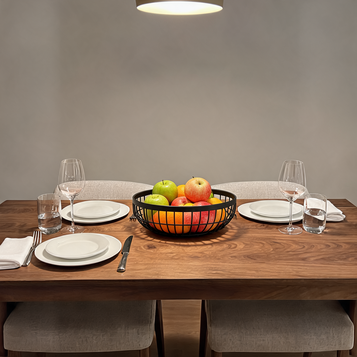 Matte black wire fruit basket on a set dining table holding apples and oranges in a single layer