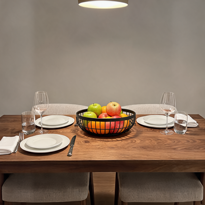 Matte black wire fruit basket on a set dining table holding apples and oranges in a single layer