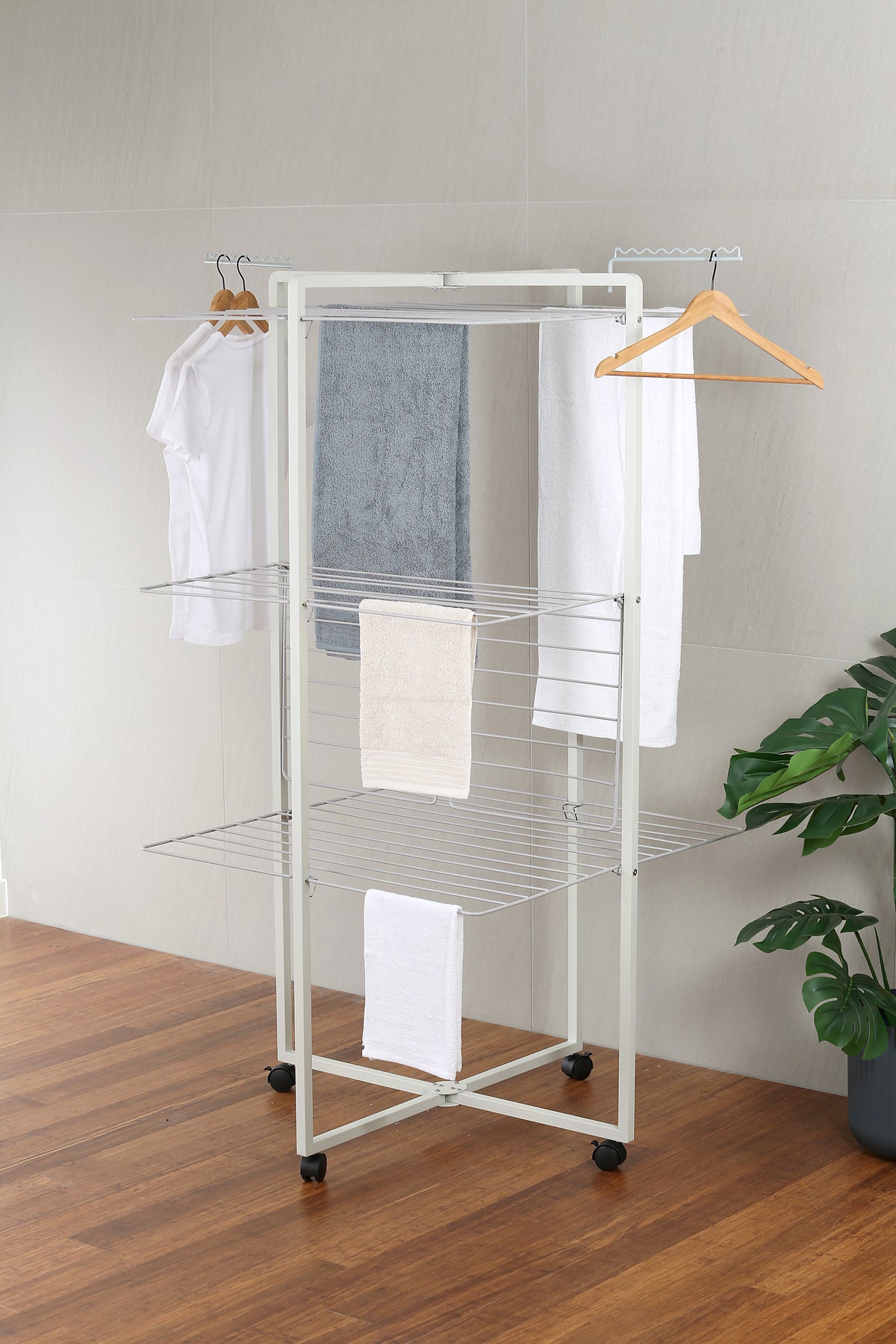 WarmyNest aluminium tower clothes airer in white, three rectangular drying tiers loaded with towels and t-shirts, both side hanging arms in use, on black castors